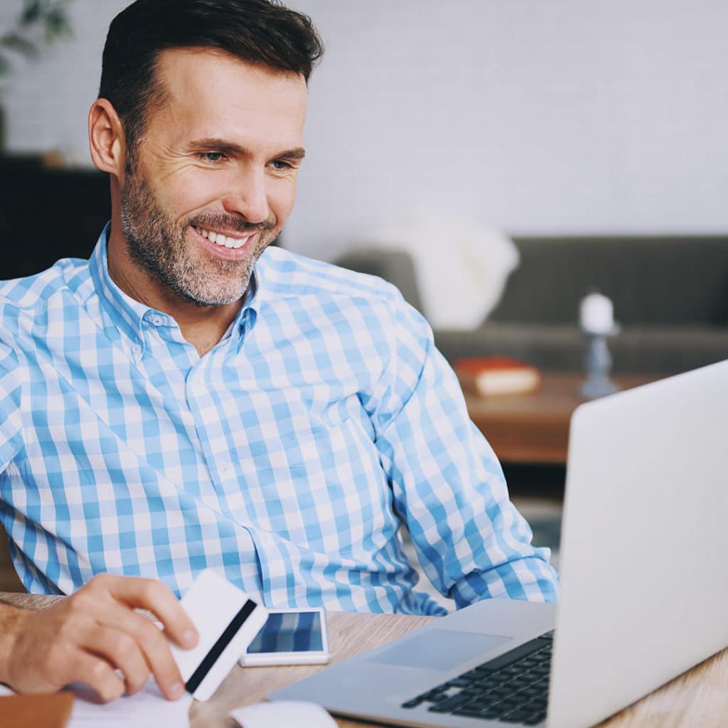 Happy man using laptop and credit card during online shopping